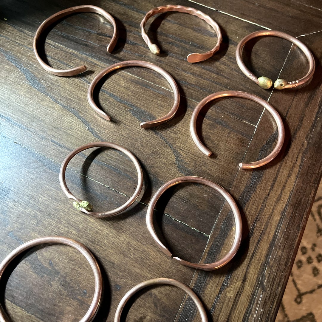 Nine hammered copper cuff bracelets laid out on wood