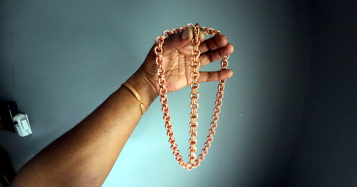 Finished slim copper rolo chain held up against gray wall